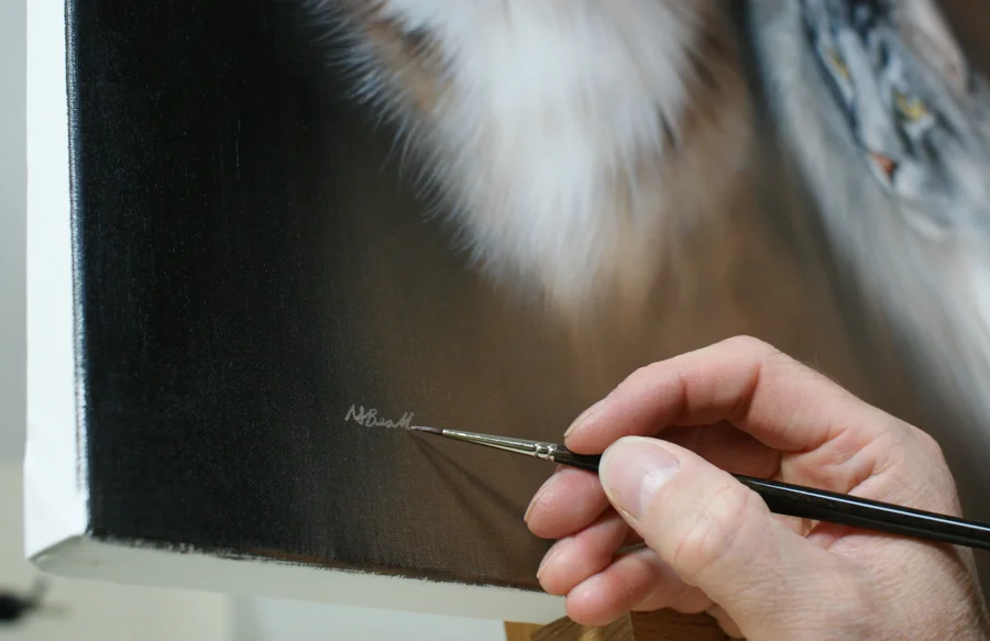 Nicholas signing his completed oil painting of a cat portrait, demonstrating the personal touch given to each artwork.
