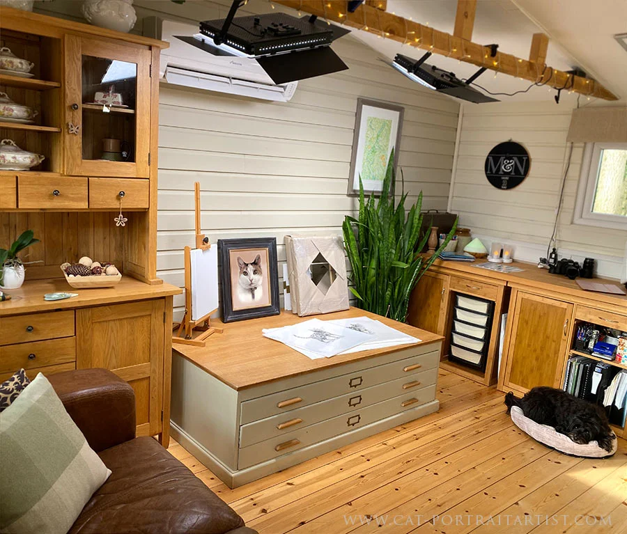 Inside the art studio, showcasing the photography light setup ready for capturing finished artwork, with Lily the Tibetan Terrier observing from her bed.