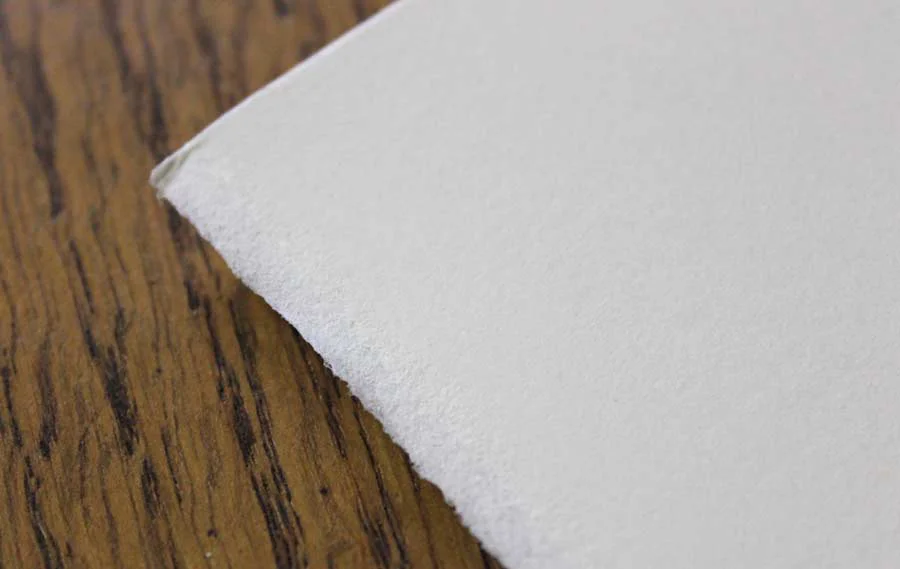 A close-up of high-quality Fabriano paper, showcasing its characteristic deckled edge and smooth, hot-pressed surface ideal for pencil portraits.