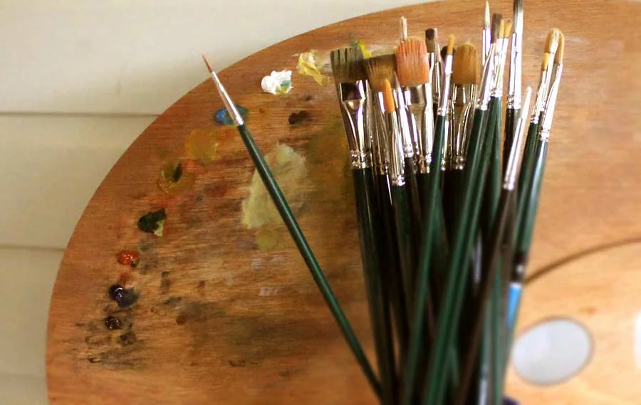 Nicholas’s well-used paint palette and a collection of brushes, showcasing the tools essential for his detailed oil pet portraits.