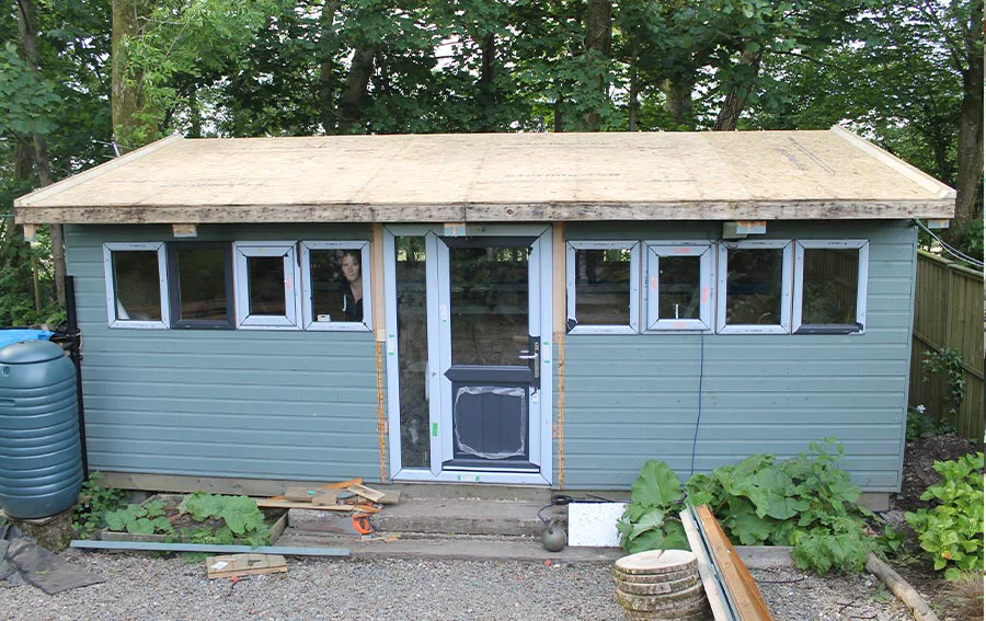 Exterior view of the renovated art studio, featuring the newly installed triple-layer felt roof, dark grey double-glazed door, and windows.