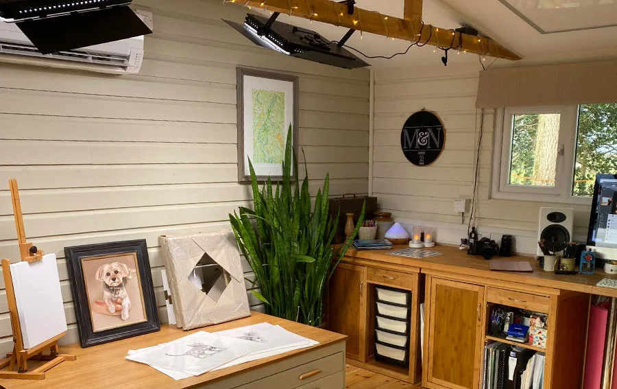 The art studio interior bathed in warm, inviting light from professional lamps and decorative fairy lights during a dark Welsh winter.